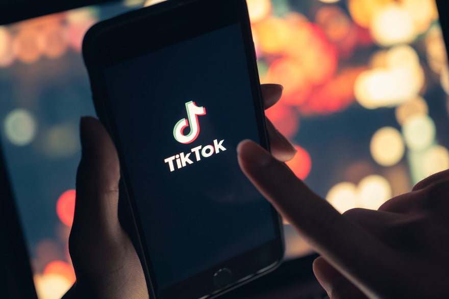 Hands holding a mobile device showing the TikTok logo on screen