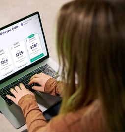 Woman using a laptop to complete an online purchase for a web builder with various prices displayed on her checkout screen