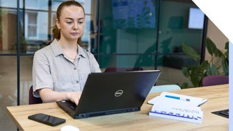 A focused professional woman working on her laptop at a modern office desk.