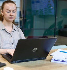 A focused professional woman working on her laptop at a modern office desk.