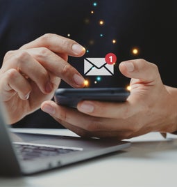 Person holding a mobile phone with a symbol for a new email floating above the device