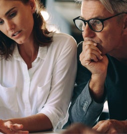 Man and woman sit at a desk looking thoughtful, discussing over sheets of paper