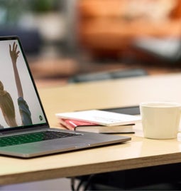 Laptop on a desk, displaying a summer Bible camp message on-screen, alongside a coffee cup and notebook on the desk.