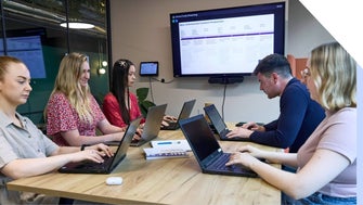 A group of professionals collaborating at a business meeting with laptops and presentation screen.