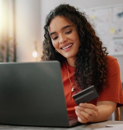 Photo of a woman at her laptop holding a credit card in her hand