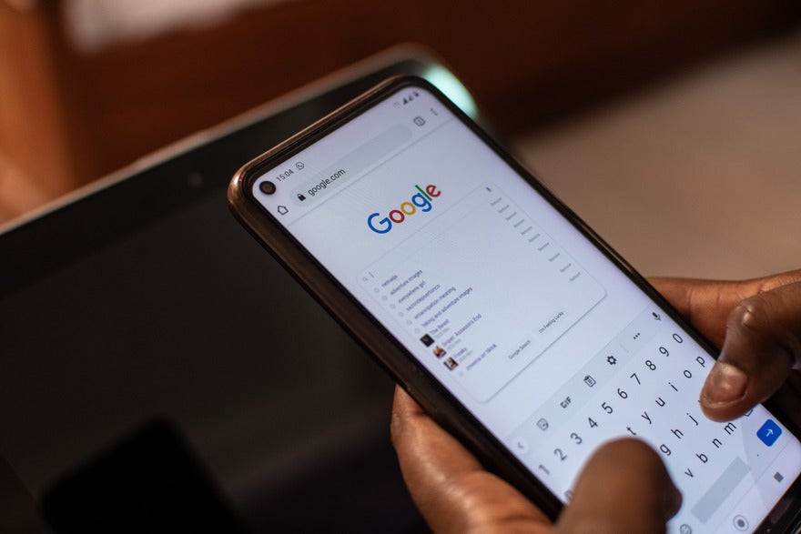 Hands holding a mobile device showing the Google homepage with a search query