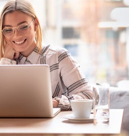 Woman sits at a desk in front of an open laptop smiling at her screen