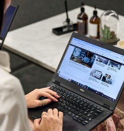 Woman in white shirt browsing her website content on a laptop in an office setting