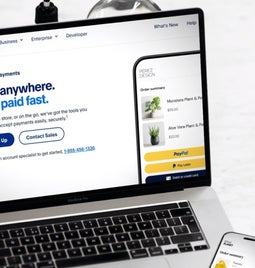 Laptop displaying PayPal's online payment options with a smartphone processing a transaction on the side.