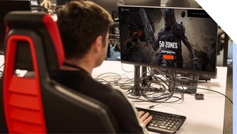 A focused gamer looks at a gaming website on a desktop setup with a Dell monitor and black-and-red gaming chair.