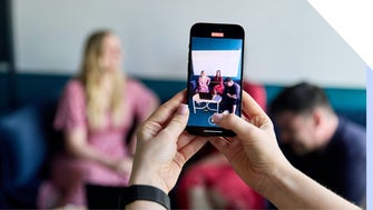 Person using a smartphone to photograph friends sitting across the table.