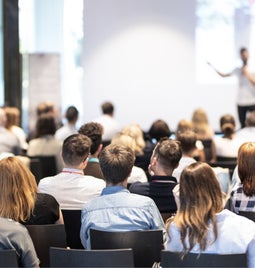 Audience of people sat in chairs listening to a speaker deliver a talk at a conference event