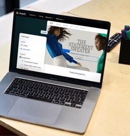 An open laptop on a wooden desk displaying a trendy online fashion store being edited in the Shopify interface.