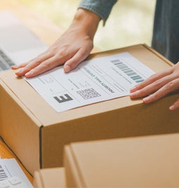 person attaching shipping label to a cardboard box on a table