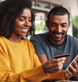 a woman holding a credit card and a phone with a man watching next to her