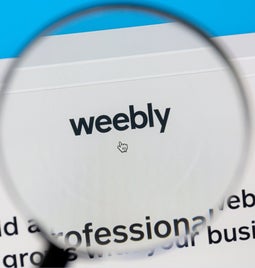 A magnifying glass hovers over a screen showing the Weebly logo