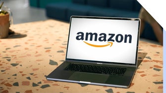 Open laptop on a patterned desk displaying a prominent Amazon logo on the screen.