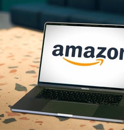 Open laptop on a patterned desk displaying a prominent Amazon logo on the screen.