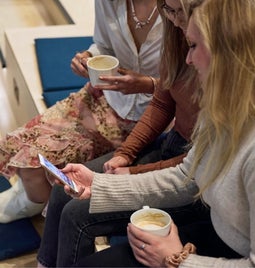 Three friends sitting and enjoying a coffee break while looking at a smartphone