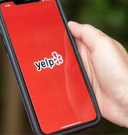 Hand holding cellphone showing Yelp logo